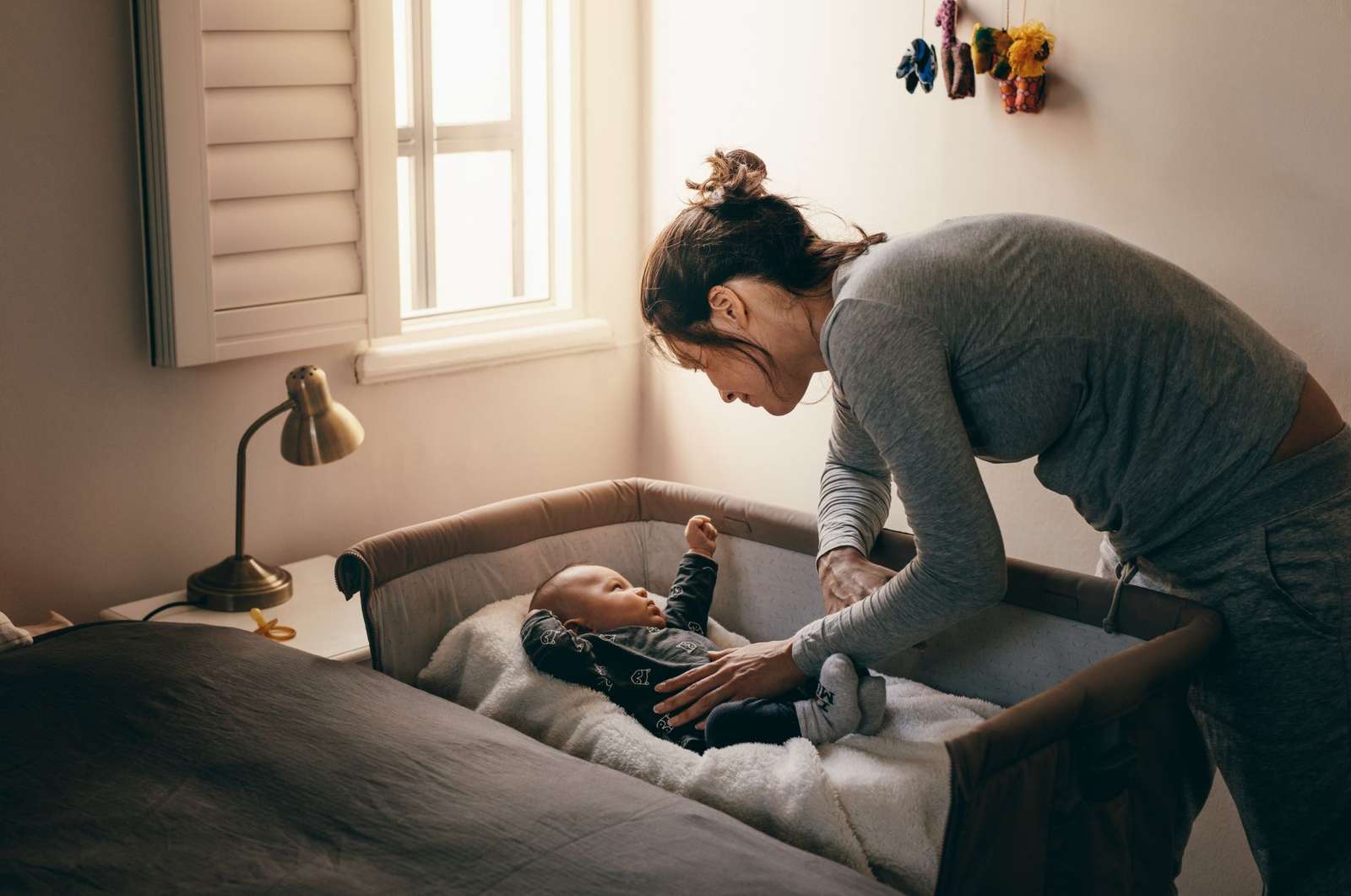 A woman gently assisting a baby in a crib