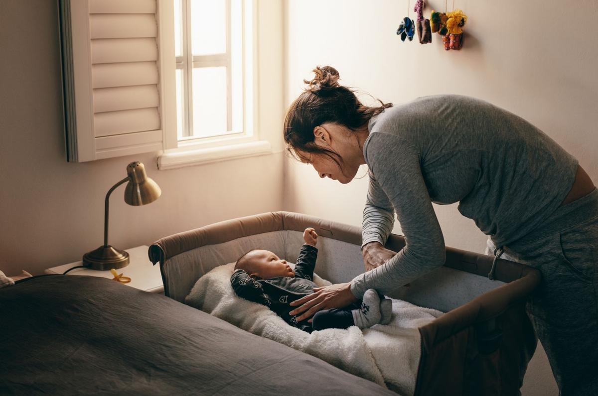 A woman gently assisting a baby in a crib