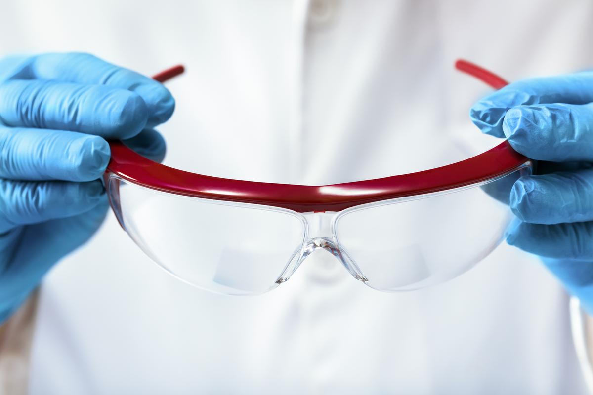 A lab technician holding a pair of safety glasses.